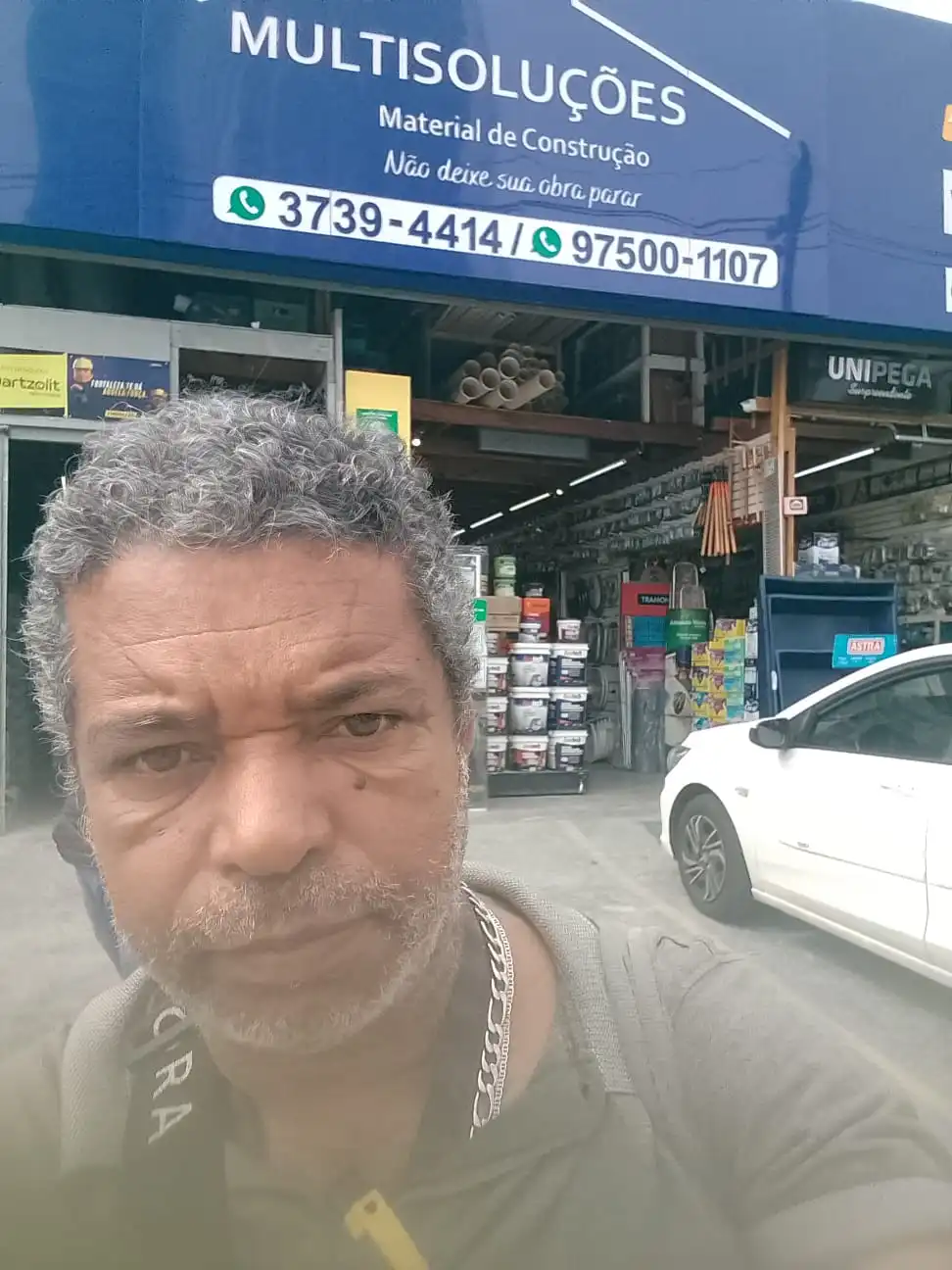 Seu Domingos Eletricista faz uma selfie em frente à loja Multi Soluções na zona oeste de São Paulo, mostrando a fachada da loja de materiais de construção. Blog Energia em Casa